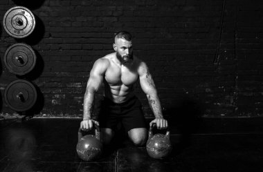Genç, aktif, terli, güçlü, kaslı bir adam spor salonunda kettlebell antrenmanına hazırlanıyor.
