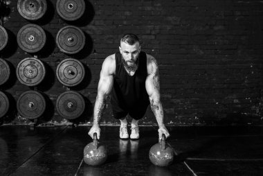 Genç, aktif, terli, formda, kaslı, kaslı bir adam spor salonundaki kettlebell 'lerde şınav çekiyor.