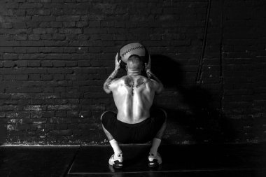 Genç, güçlü, terli, formda, kaslı, iri kaslı bir adam spor salonunda sıkı antrenman yapmak için duvarlara ilaç topu atıyor.