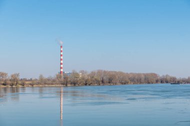 Arka planda mavi gökyüzü olan bir su ısıtma tesisi ya da elektrik santrali bacası.