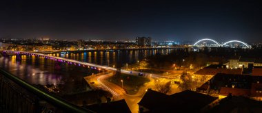 Night panoramic view of Novi Sad, Serbia cityscape with bridges, Danube river and Petrovaradin fortress with beautiful colorful street lights from the town clipart