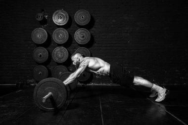 Genç, güçlü, kaslı, terli, kaslı, spor salonunun zemininde halter sallayarak kas çalıştıran güçlü bir adam.