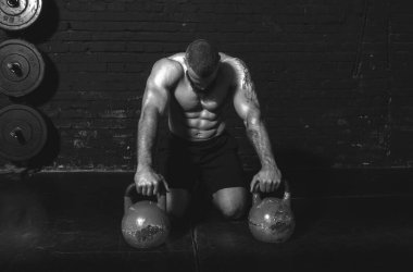 Genç, aktif, terli, güçlü, kaslı bir adam spor salonunda kettlebell antrenmanına hazırlanıyor.