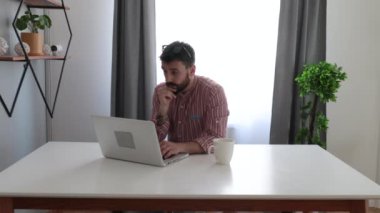 Ofisindeki masasında oturan serbest çalışan genç bir adam dizüstü bilgisayar kullanarak şirketinin yeni projesinde fazla mesai yapıyor. 