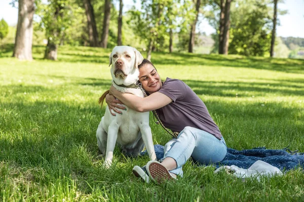 年轻美丽的女人坐在公园里 抱着她的宠物狗 金色的拉布拉多猎犬 和她的朋友一起享受着阳光灿烂的天气 — 图库照片