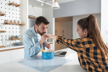 Mutlu genç çift akşam yemeği için mutfakta makarna pişirirken ve internetten yemek tarifleri okurken eğleniyor.
