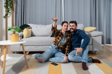 Genç çift evlerinin zemininde oturup TV 'de aşk filmi izlerken, kadın ona sahnenin tadını çıkarıyor ve o da yüzünde sahte bir gülümsemeyle ilgileniyormuş gibi yapıyor.