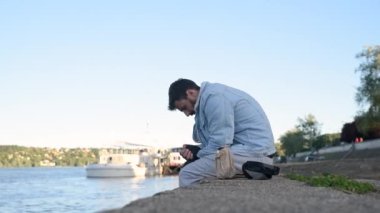 Genç, hasta, umutsuz ve depresif evsiz bir adam şehirdeki rıhtımlarda oturuyor ve sarhoş olmak için alkol içiyor üzgün ve insanlardan terk edilmiş hissediyor, sosyal belgesel kavramı.