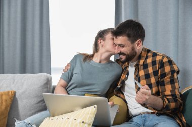 Evlerindeki genç çift, doğum günü için dizüstü bilgisayardan yeni akıllı telefon sipariş ederek ve kredi kartıyla ödeme yaparak ve kız arkadaşının onu yanağından öpmesiyle sevgilisine sürpriz yapıyor.