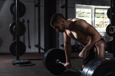 Genç, güçlü, terli, aktif vücut geliştirici, halterci, kaslı, spor salonunda ağır antrenmanlara ara veren, ölü kaldırma hareketleri yaptıktan sonra nefes alan kaslı adam.