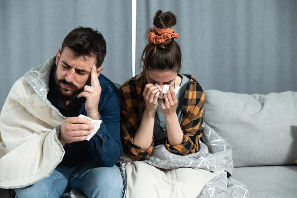 这对年轻夫妇患有感冒和流感 他们坐在家里 裹着毛毯 用纸巾擦拭鼻子 而他们却有着强烈的头痛和健康观念 — 图库照片