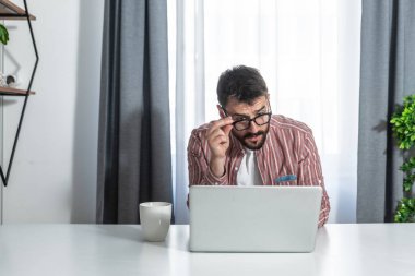 Genç başarılı serbest çalışan adam, evde çalışırken bilgisayarındaki e-postaları ve borsa istatistiklerini okuyor.