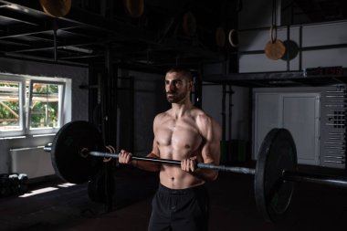 Genç, aktif, terli, kaslı, iri kaslı, kaslı, spor salonunda halterli, kıvrımlı, güçlü bir adam.