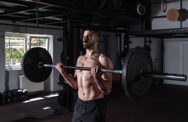 Genç, aktif, terli, kaslı, iri kaslı, kaslı, spor salonunda halterli, kıvrımlı, güçlü bir adam.