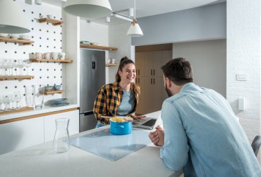 Genç mutlu çift mutfakta durup yemek pişiriyor. İnternette buldukları tarifleri kullanıyorlar.