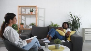Ofiste bir psikoterapistle oturan genç siyahi kadın depresyon ve anksiyete sorununu çözmek için terapi seansı yapıyor.