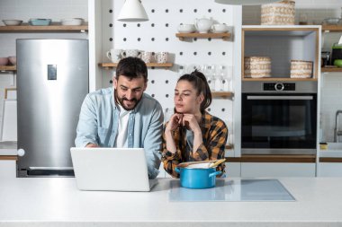 Genç adam ciddi kız arkadaşına sataşıyor ve ona bir yemek tarifi ve nasıl görünmesi gerektiğine dair bir fotoğraf gösteriyor ve ona mutfakta dururken yemek yapmayı bilmediğini söylüyor.