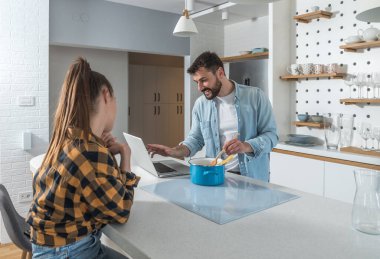 Genç ve mutlu bir çift, yemek pişirmek için dizüstü bilgisayarlarında yemek tarifleriyle çevrimiçi kurs izliyor.