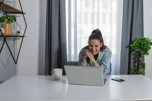 Young happy smiling woman standing in her home office talking on the video call via internet using laptop web cam with her boyfriend who is in the military on the assignment in the different country