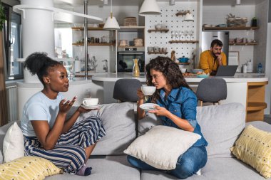 Genç melez aile, bir fincan çay eşliğinde arkadaşlarını misafir olarak ağırladı. Kadınlar konuşurken erkekler çalışmak zorundalar. O ise mutfakta dizüstü bilgisayarıyla iş yapıyor.