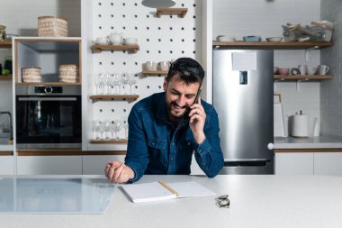 Genç ve başarılı bir iş adamı modern bir mutfakta evde duruyor ve bir teslimat şirketi ile akıllı bir telefonla konuşuyor. Her zaman onlardan sipariş verecek memnun bir müşteri olarak.