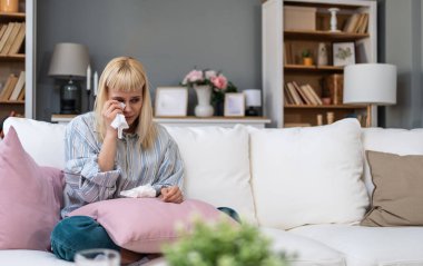 Genç bir kadın kanepede ağlıyor, mendil tutuyor ve yastığa sarılıyor, kalp kırıklığını işliyor, endişe ve keder, nefes alma egzersizleri yapıyor, terapiyi düşünüyor ve bir arkadaşına destek araması için mesaj atıyor.