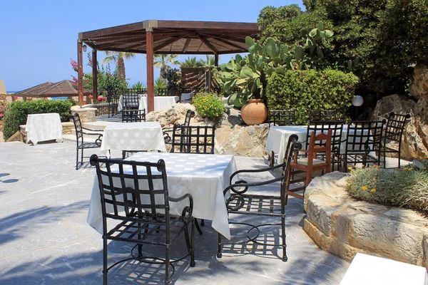 Tables and iron chairs on terrace and beautiful garden, Crete — Stock Photo, Image