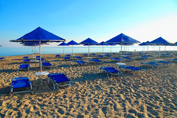 Ombrelloni blu e chaise longue sulla spiaggia di sabbia vuota, Grecia — Foto Stock