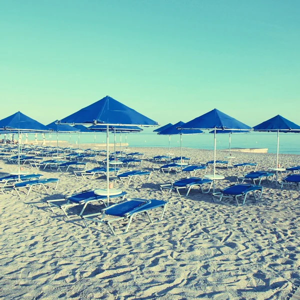 Guarda-chuvas azuis e chaise longue na praia de areia vazia, Grécia — Fotografia de Stock