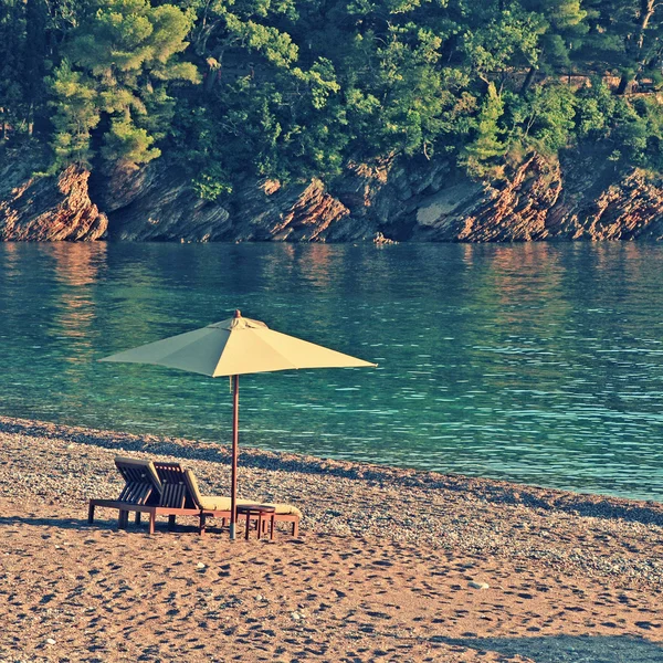 Dos tumbonas y sombrilla en la playa en la bahía rocosa . — Foto de Stock