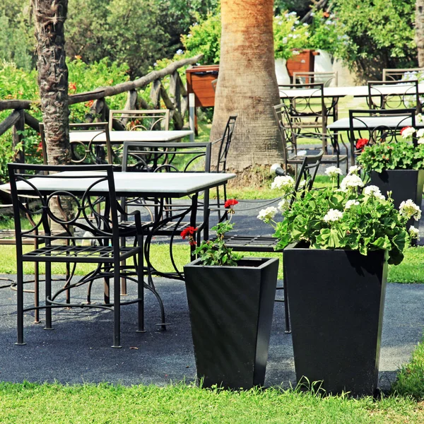 Tafels, stoelen van ijzer en bloempotten in tuin (Griekenland) — Stockfoto