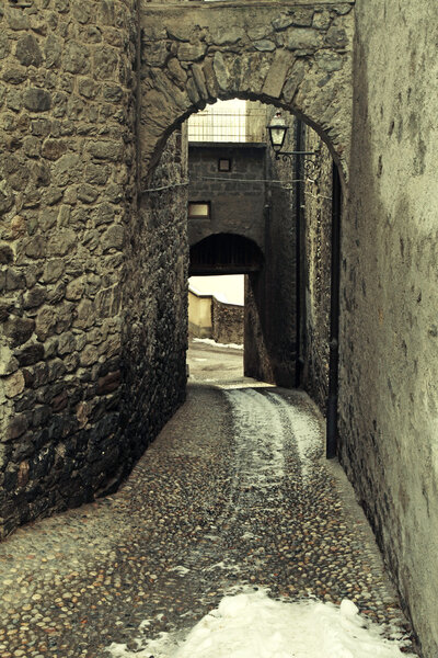 Rustic arched street in a old alpine village, Italian Alps, vintage toned image