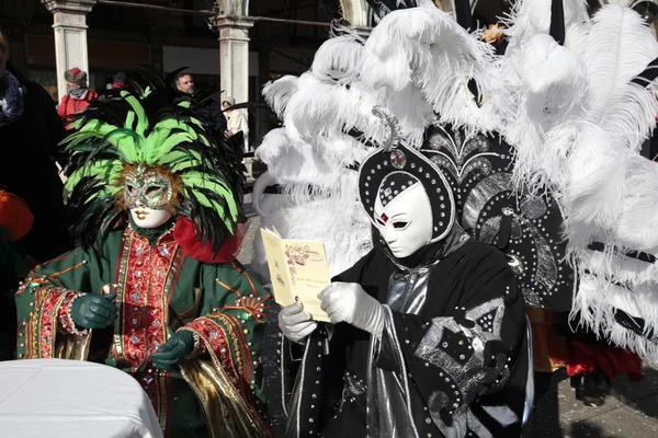 Masked persons in colorful costume with plumage sitting in cafe, Venice, Italy