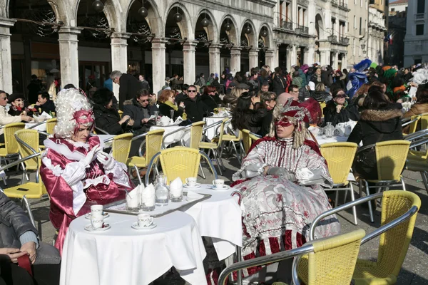 Turistas y personas enmascaradas en traje colorido sentado en la cafetería —  Fotos de Stock