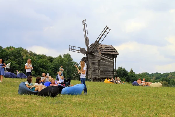 People relax on grass near old wooden mill in Museum Pirogovo, Kiev — 스톡 사진