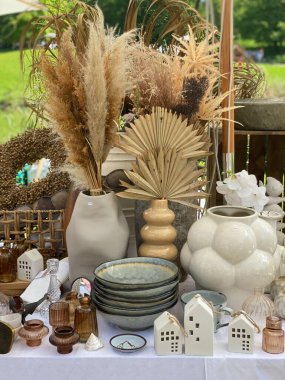 Açık hava pazarındaki bir masada yumuşak gri-bej tonlarda dekoratif nesneler. Minimalist el yapımı seramik ve klasik ev dekorasyonu sakin, zarif ve nötr bir estetik yaratıyor..