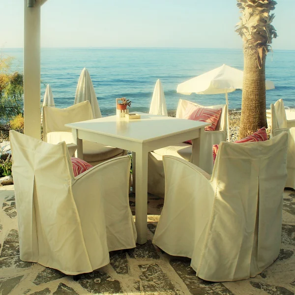 Mesas e cadeiras brancas no café grego pela costa do mar, Grécia — Fotografia de Stock