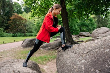 Genç kız parkta esneme hareketleri yapıyor.