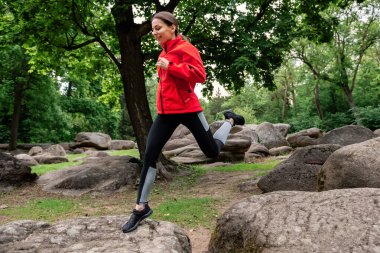 Genç kız parkta taştan taşa zıplıyor.