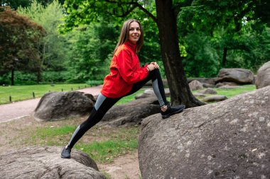 Genç kız parkta esneme hareketleri yapıyor.