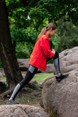 Genç kız parkta esneme hareketleri yapıyor.