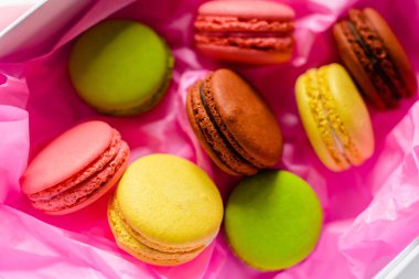 çok renkli badem kurabiyeleri pembe kağıt arka planda bir karton kutunun üzerinde