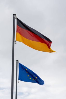 LEER, ALMANY - 11 Eylül 2025: Almanya 'nın ulusal bayrağı ve Avrupa Birliği bayrağı bulutlu gri gökyüzüne doğru bayrak sallıyor.