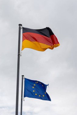 LEER, ALMANY - 11 Eylül 2025: Almanya 'nın ulusal bayrağı ve Avrupa Birliği bayrağı bulutlu gri gökyüzüne doğru bayrak sallıyor.