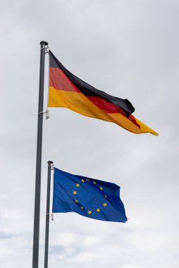 LEER, ALMANY - 11 Eylül 2025: Almanya 'nın ulusal bayrağı ve Avrupa Birliği bayrağı bulutlu gri gökyüzüne doğru bayrak sallıyor.