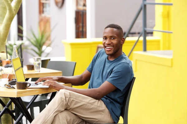 Усміхнений хлопець сидить у кафе з ноутбуком — стокове фото