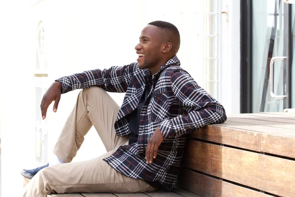 Šťastný mladý muž sedí na lavičce — Stock fotografie