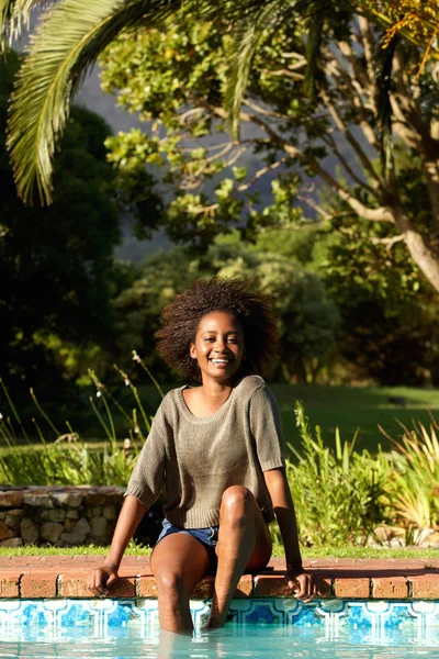 Smiling black woman sitting by pool — Stock Photo, Image