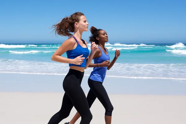 Zwei junge Frauen laufen am Strand entlang — Stockfoto