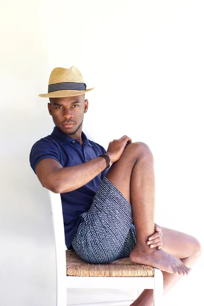 Unga afrikanska killen med hatt sitter på en stol — Stockfoto